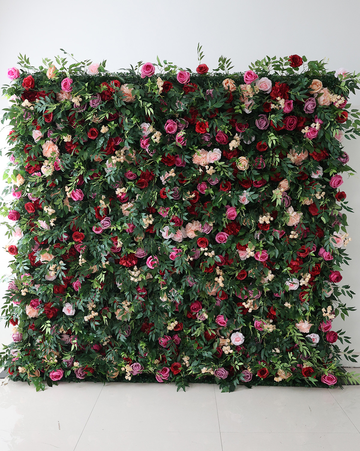 Lush green flower wall rental with red, pink, purple, and peach roses