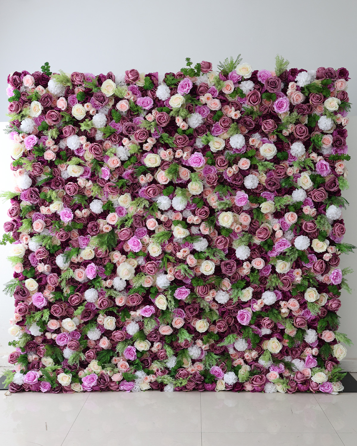 Flower wall rental with purple, peach, and white roses with green shrubbery